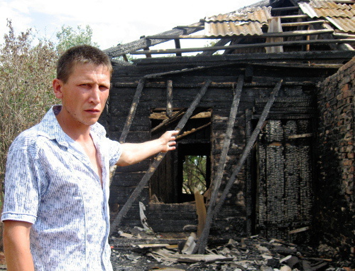 Виталий Богданов показывает наполовину сгоревший барак и кирпичную стену справа, которая спасла их квартиру от огня. Астрахань, Приволжский район, поселок Стеклозавода, 19 июня 2012 г. Фото Вячеслава Ященко для "Кавказского узла"
 