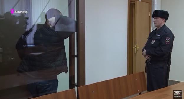 Муслим Джамбеков (за стеклом) в суде. Скриншот с видео "Предполагаемый виновник смертельного ДТП Муслим Джамбеков арестован на два месяца" пользователя Телеканал 360  на Youtube, https://www.youtube.com/watch?v=XyyCD7r_g64