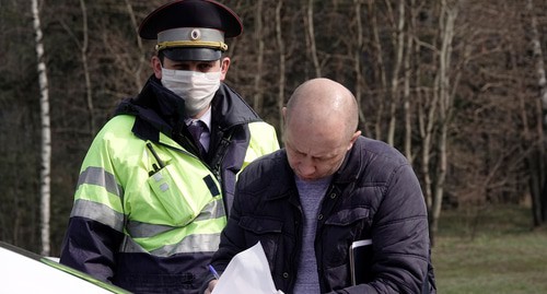 Мужчина заполняет документы рядом с сотрудником ГИБДД в защитной маске на контрольно-пропускном пункте. Фото REUTERS/Tatyana Makeyeva