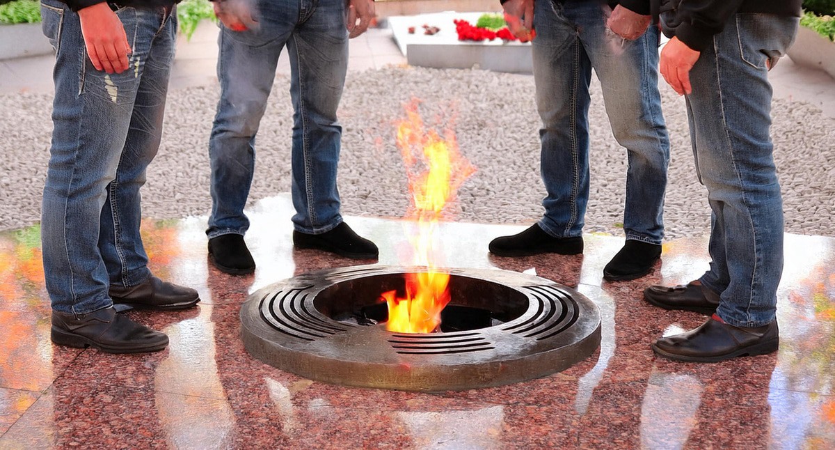 Мужчины стоят у Вечного огня. Иллюстрация создана «Кавказским узлом» с помощью ИИ в программе Photoshop
